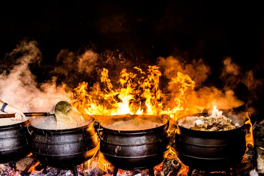 Cooking *something* in 4 dark pots (perhaps cauldrons) in front of open flame.