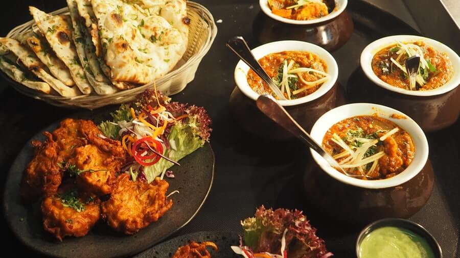 Indian Food: butter and garlic naan, pakora, curries (butter chicken, I hope), and mint chutney laid out on a table.